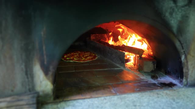 4K披萨在传统砖披萨烤箱。厨师在厨房用肉、奶酪和蔬菜制作披萨面团，为意大利餐厅的顾客服务。意大利食物和餐厅的概念视频素材
