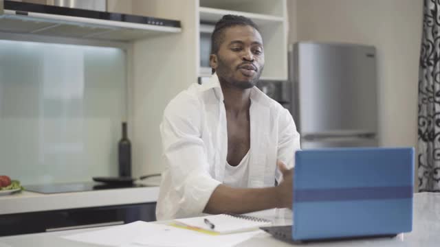 自信的商人在厨房里使用视频聊天的肖像。年轻英俊的非裔美国人在网上工作。商业生活方式的概念。视频素材