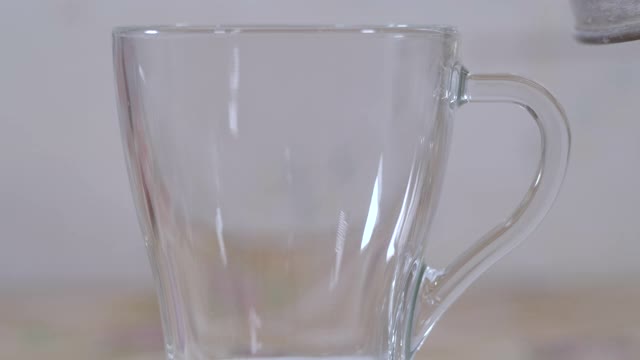 慢镜头特写倒热水到玻璃杯里，为茶或咖啡在厨房。泡茶，热水从茶壶倒进杯子，蒸汽从杯子冒出来，玻璃上有水滴。视频素材
