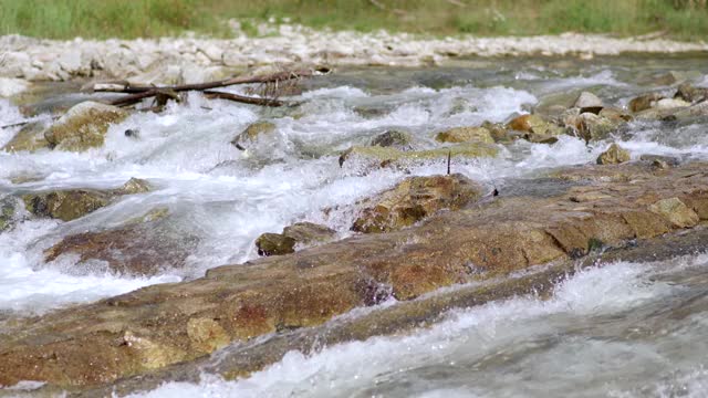 河流在阳光明媚的日子里流过岩石，近距离的细节，快速的白水与模糊的石头和草的背景视频素材
