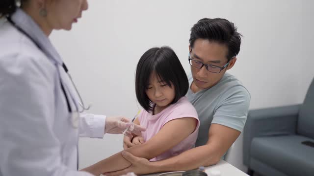 亚洲华人女医生在诊所给孩子打针。小女孩在打针时又喊又哭。她的父亲帮助抚养和照顾他的女儿们。视频素材