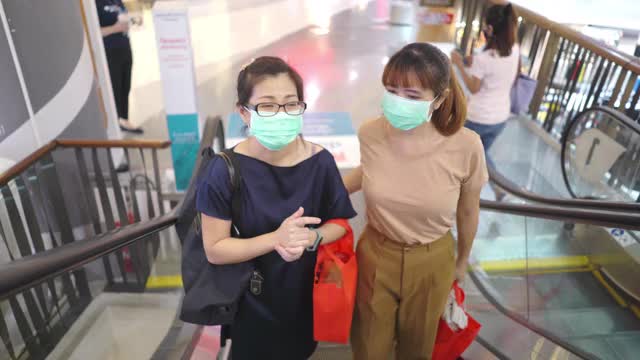 在购物中心的自动扶梯上，两名亚洲妇女戴着防护口罩视频素材