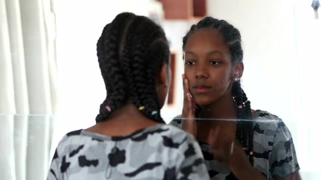 十几岁的黑人女孩看着镜子里的自己。青春期的非洲女孩检查脸视频素材
