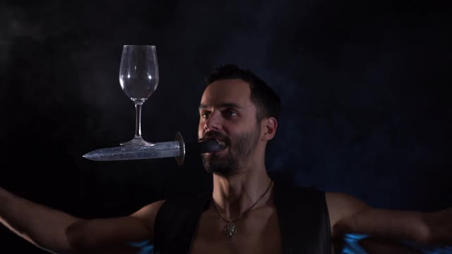 一个男人嘴里叼着一把刀，摇晃着，保持着杯子的平衡。独特的马戏团的技能。视频下载
