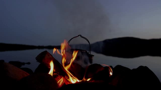 晚上在湖边的营火上用钢制水壶烧水。视频素材