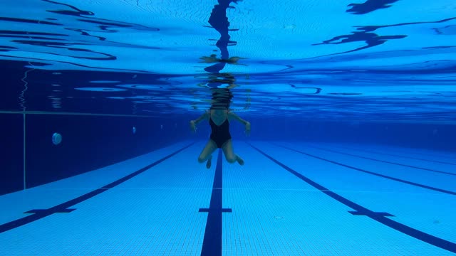 低角度观看亚洲华裔女游泳运动员游过游泳池视频素材