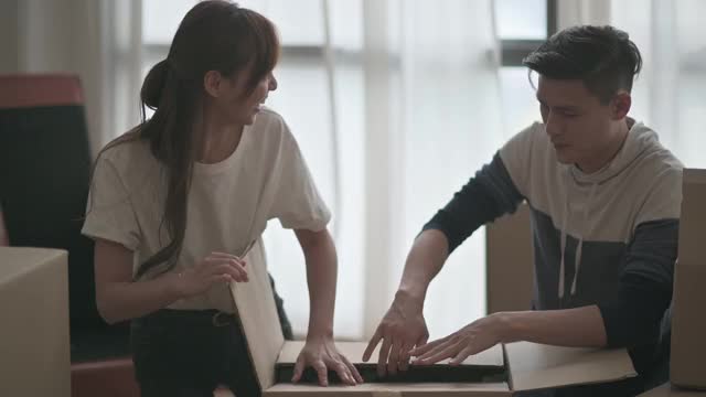 亚洲华人夫妇切割和打开纸板箱在客厅视频下载