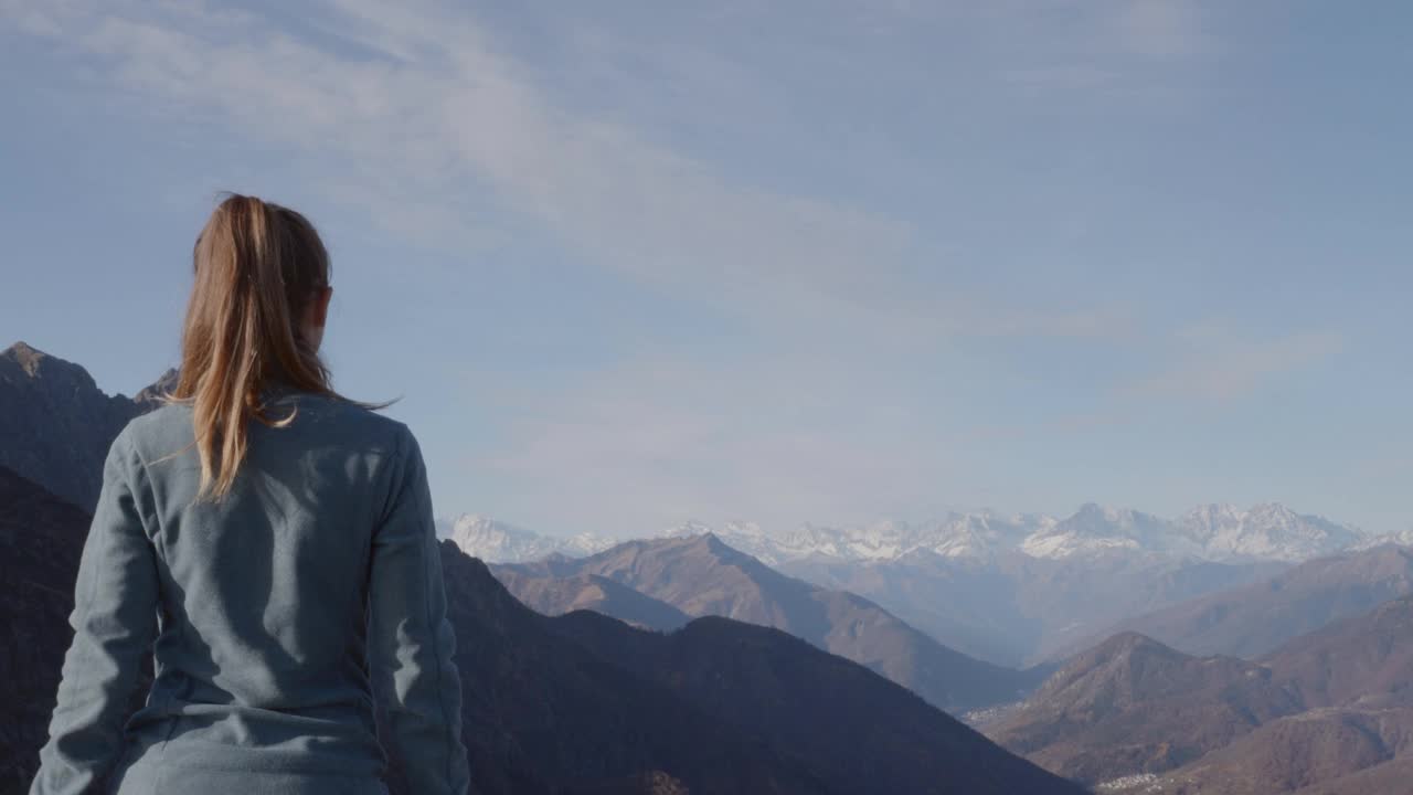 女徒步旅行者站在山顶，双臂张开。年轻女子在徒步旅行中举起双臂俯瞰壮观的山脉视频素材
