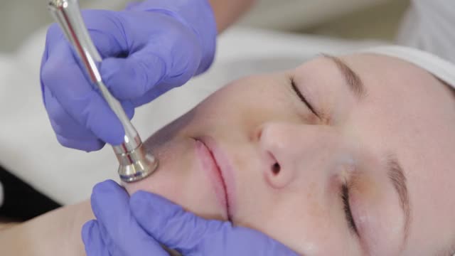 女性美容师在客户的脸上进行皮肤磨皮美容程序视频素材