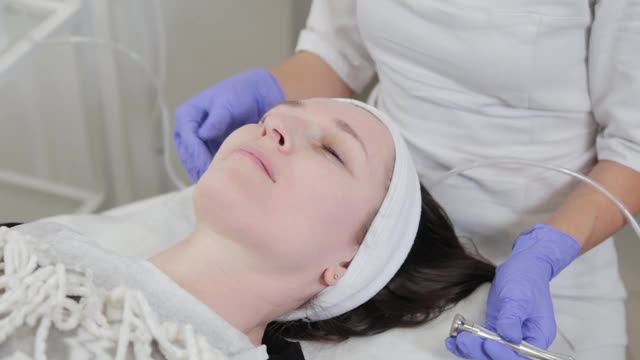 女性美容师在客户的脸上进行皮肤磨皮美容程序视频素材