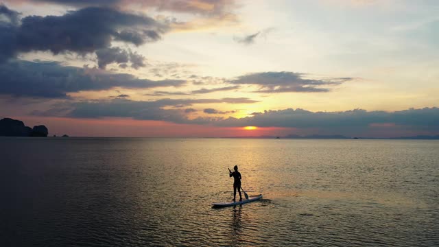 4K无人机航拍剪影的信心亚洲妇女站在sup板与桨板通过在夏季日落的海上。女性在假期喜欢水上娱乐运动视频素材