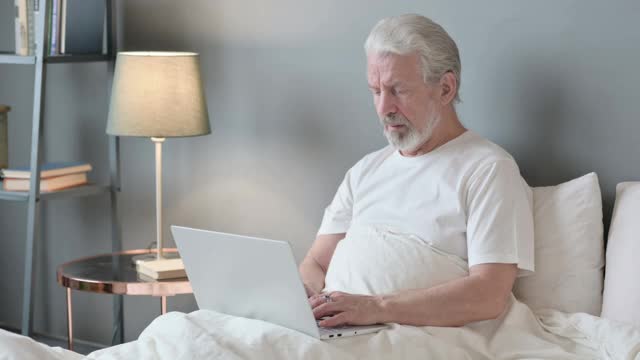 带着笔记本电脑的老人在床上背痛视频素材