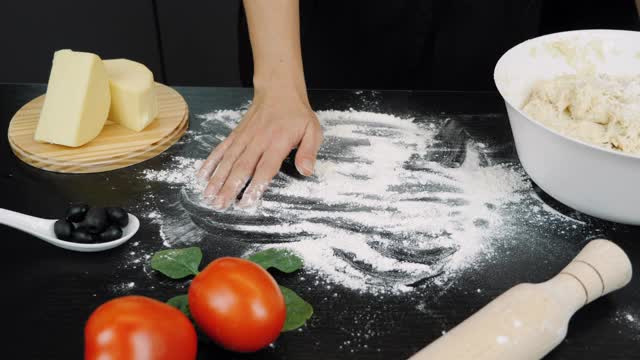 一个女人正在家里做手工披萨。厨师的手往桌上撒面粉。烘焙用酵母面团的制备工艺视频素材