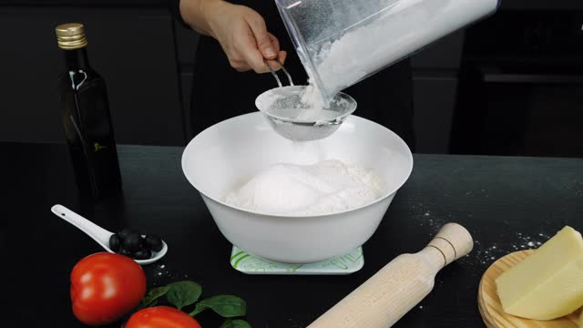 在厨房里准备面粉来烤披萨。面粉正在过筛。白面粉正从筛子上磨碎。筛面粉烘焙视频素材