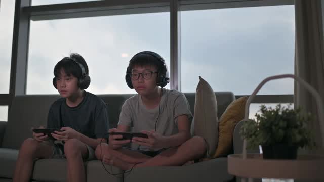 两个华裔少年放学后在客厅玩手机游戏视频素材