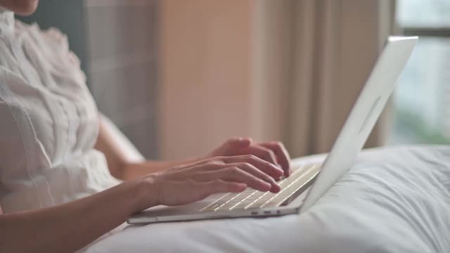 一个成熟的亚洲华裔女性，在家里用笔记本电脑和智能手机在卧室工作视频下载