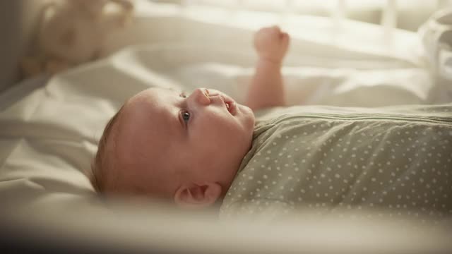 一个可爱的新生儿躺在婴儿床上的真实近距离镜头。在舒适的家空间一个高加索新生儿的顽皮肖像。童年、新生活和为人父母的概念。视频素材