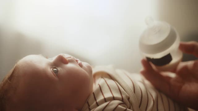 真实的近距离镜头，一个新生儿喝牛奶从小婴儿瓶，而躺在儿童床上。家庭中的白人新生儿的肖像。儿童与父母的概念。视频素材