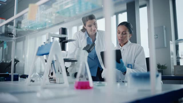 现代医学研究实验室:两位女科学家使用显微镜一起工作，分析样本，交谈。医学、生物技术开发高级科学制药实验室视频素材