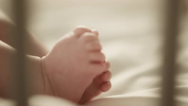 一个可爱的新生儿躺在婴儿床上的真实近距离镜头。白种婴儿的小人类脚在焦点。童年、新生活和为人父母的概念。视频素材