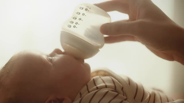 真实的近距离镜头，一个新生儿喝牛奶从小婴儿瓶，而躺在儿童床上。家庭中的白人新生儿的肖像。儿童与父母的概念。视频素材