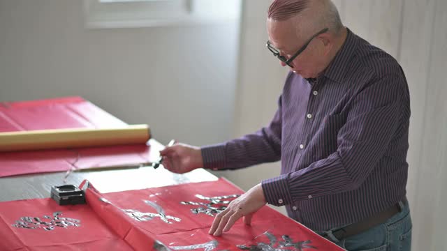 亚洲华人男性练习书法，为即将到来的中国新年庆祝家庭装饰目的与繁荣和良好的措辞写在一张红色的纸上视频素材