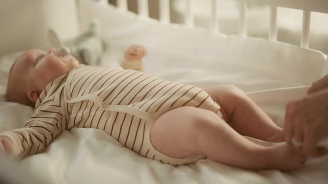 真实的近距离镜头母亲安抚和轻轻按摩一个新生儿在婴儿床。在孩子卧室的白种人新生儿蹒跚学步。童年、新生活和为人父母的概念。视频素材