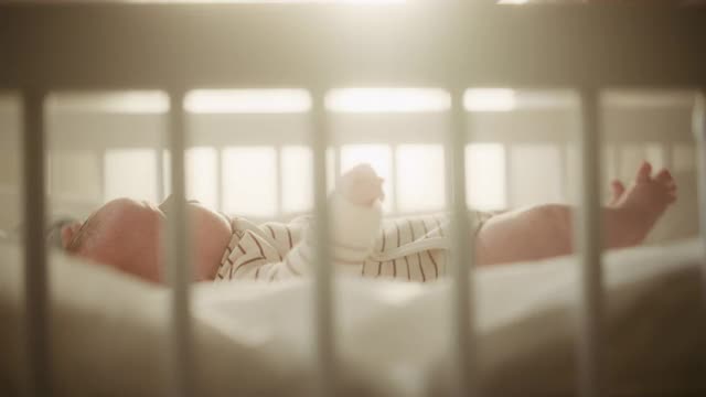 一个可爱的新生儿躺在婴儿床上在舒适温暖明亮的房间里的真实镜头。快乐的妈妈从卧室接新生儿。童年的概念，新生活，为人父母。视频素材