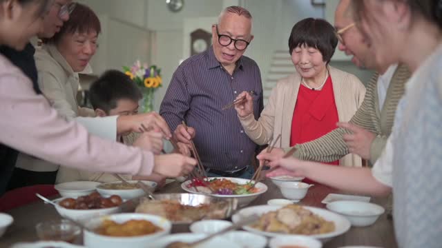 亚洲华人多代家庭庆祝中国新年前夕与传统食物娄桑(生鱼菜肴)团圆饭视频购买