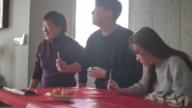 亚洲华人家庭在红纸上书写中国书法，以求繁荣，准备中国新年的家庭装饰视频购买