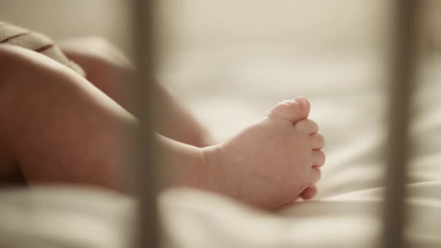 一个可爱的新生儿躺在婴儿床上的真实近距离镜头。白种婴儿的小人类脚在焦点。童年、新生活和为人父母的概念。视频素材
