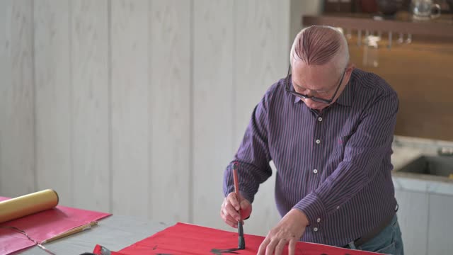 亚洲华人男性练习书法，为即将到来的中国新年庆祝家庭装饰目的与繁荣和良好的措辞写在一张红色的纸上视频素材