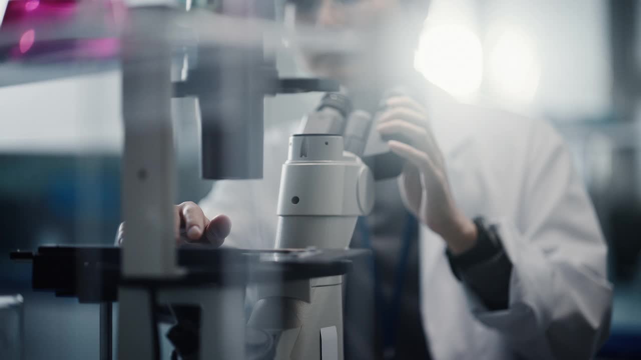医学发展实验室:东亚科学家在显微镜下观察的肖像，分析培养皿样本。大型制药实验室从事医学、生物技术、微生物学、药物研究视频下载