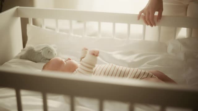 一个可爱的新生儿躺在婴儿床上在舒适温暖明亮的房间里的真实镜头。快乐的妈妈从卧室接新生儿。童年的概念，新生活，为人父母。视频素材
