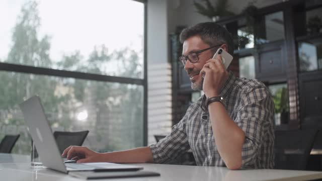 年轻英俊的大胡子男子坐在家里用笔记本电脑打电话。男性自由职业者在家里用电脑与客户通话视频素材