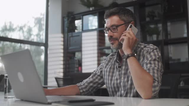 年轻英俊的大胡子男子坐在家里用笔记本电脑打电话。男性自由职业者在家里用电脑与客户通话视频素材