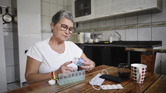 一位年长的女士正在把药品放在每日的药品收纳器里视频下载