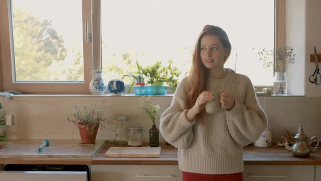 一个女人拿着杯子站在厨房里视频素材