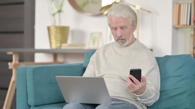 老人在沙发上用智能手机和笔记本电脑工作视频素材