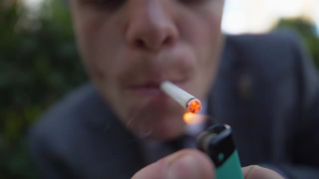 一个穿西装的年轻人点燃了一根烟，超级近距离的男人正在抽烟视频素材