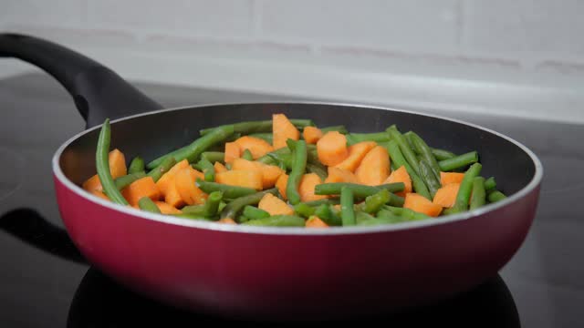 在煎锅里炒胡萝卜和菜豆的特写。烹饪素食视频素材