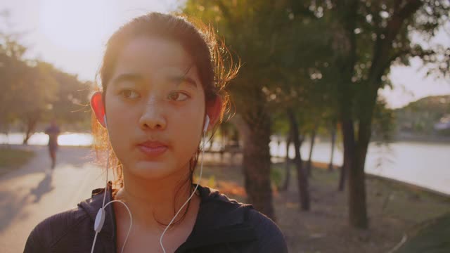 迷人的亚洲少女听音乐，同时在公园里跑步。年轻女子晨跑锻炼。视频素材