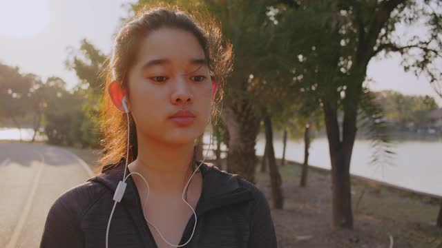 迷人的亚洲少女听音乐，同时在公园里跑步。年轻女子晨跑锻炼。视频素材