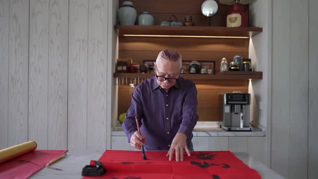 亚洲华人爷爷在中国新年期间练习书法，家里装饰一张红色的纸视频下载