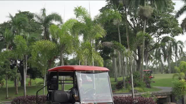 年轻的亚洲华人男子高尔夫球驾驶高尔夫球车和拆包设备在高尔夫球场视频下载