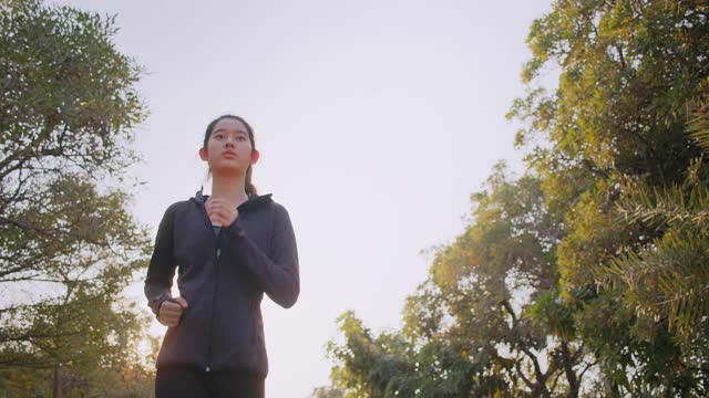 迷人的亚洲少女在公园里跑步。年轻女子晨跑锻炼。视频素材