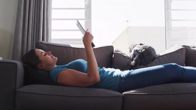 一个白人女人躺在沙发上，狗在用数码平板电脑视频素材