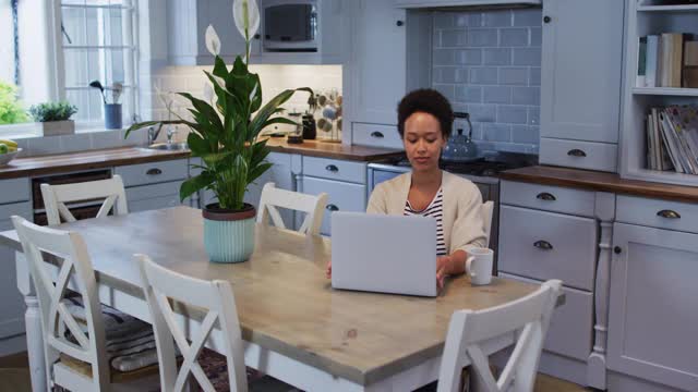 混血女性使用笔记本电脑，在厨房喝咖啡视频素材