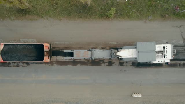 把旧沥青和附近路过的汽车一起卸载到卡车上。道路建设机械视频下载