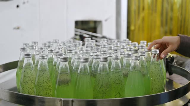 绿色果汁瓶在生产线上旋转，检验员在饮料加工厂手工检查产品视频素材
